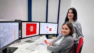 Ausbilderin und die Lernende Polygrafin prüfen einen Farbton auf einem Druckbild.