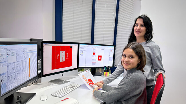 Ausbilderin und die Lernende Polygrafin prüfen einen Farbton auf einem Druckbild.