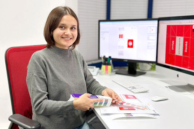 Lernende Polygrafin sitzt am Schreibtisch und hat einen Farbfächer in der Hand.