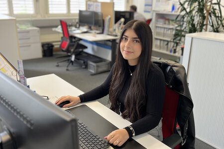 Eine Kauffrau Lernende, die am Arbeitsplatz vor ihrem Bildschirm sitzt. (