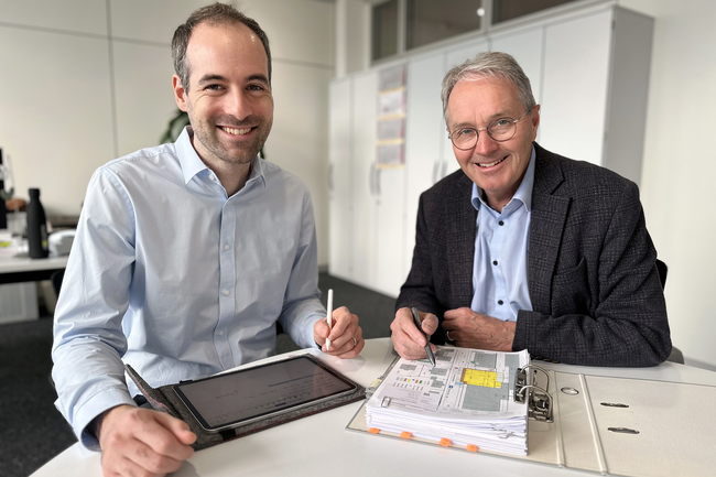 Thomas Hansmann (rechts) mit Pascal Graf vor einem Grundriss am Tisch sitzend