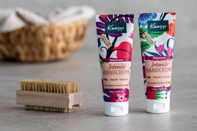Neben einer Handbürste stehen zwei Kosmetiktuben für Handcreme.