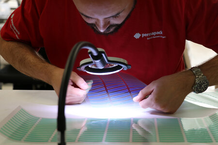 Mitarbeiter prüft Formstanzteile unter einer Lampe