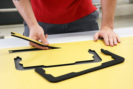 Mitarbeiter löst geschnittene Formstanzteile aus Kunststoff aus der Grundplatte.