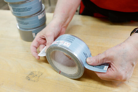 Eine Etikette wird auf eine Rolle graues Klebeband aufgeklebt