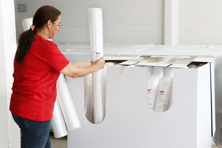 Eine Mitarbeiterin platziert längliche weisse Rollen in eine Kartonschachtel