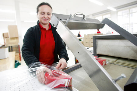 Eine Mitarbeiterin legt eine rote Klebebandabrolle in einen Plastikschlauch zum anschliessenden Schrumpfen.