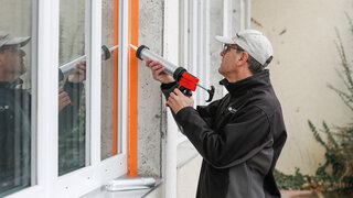 Arbeiter dichtet eine Fenster-Anschlussfuge im Freien mit Dichtmasse ab.