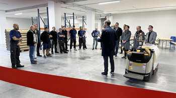 Mitarbeitende stehen bei der Ansprache zur Einweihung im Halbkreis. 