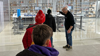 Eine Gruppe Kinder schaut durch einen transparenten Vorhang in den Reinraum für Formstanzteile.