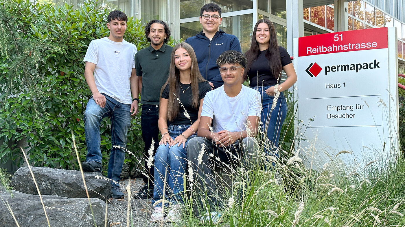 Sechs Lernende stehen neben dem Permapack-Firmenschild. 