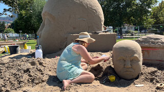 Sandkünstlerin sitzt im Sand und arbeitet an ihrer Skulptur.