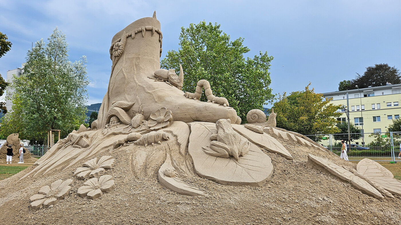 Sandskulptur: Insekten, Käfer und Amphibien auf, unter und neben einem menschlichen Fuss.
