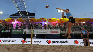 Beachvolleyballerin bei einem Schmetterball von unten fotografiert, im Hintergrund die Bande mit Permapack-Logo.