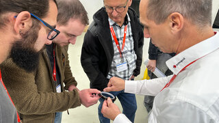 Teilnehmende stehen in einer Runde und begutachten ein frisch zugeschnittenes Polyimid-Klebeband.