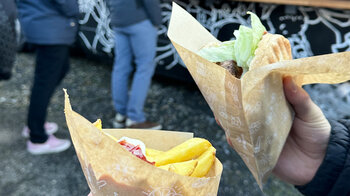 Ein frisch gemachter Burger und eine Tüte Pommes in den Händen eines Teilnehmers.