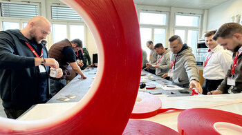 Klebeworkshop: Einige Teilnehmer stehen um einen Arbeitstisch.