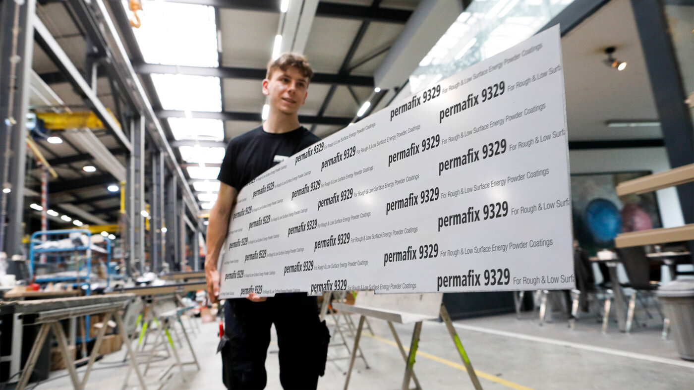 Metallbauer trägt eine Metallplatte, dessen Oberseite mit einer Schutzfolie beklebt ist.