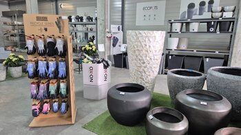 Auf dem Boden stehen Pflanzgefässe und in einem Karton-Regal hängen verschiedene Arbeitshandschuhe.