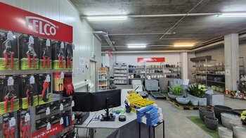 Im Vordergrund steht ein Regal mit Gartenwerkzeugen und im Hintergrund gibt es Regale mit Pflanzgefässen.