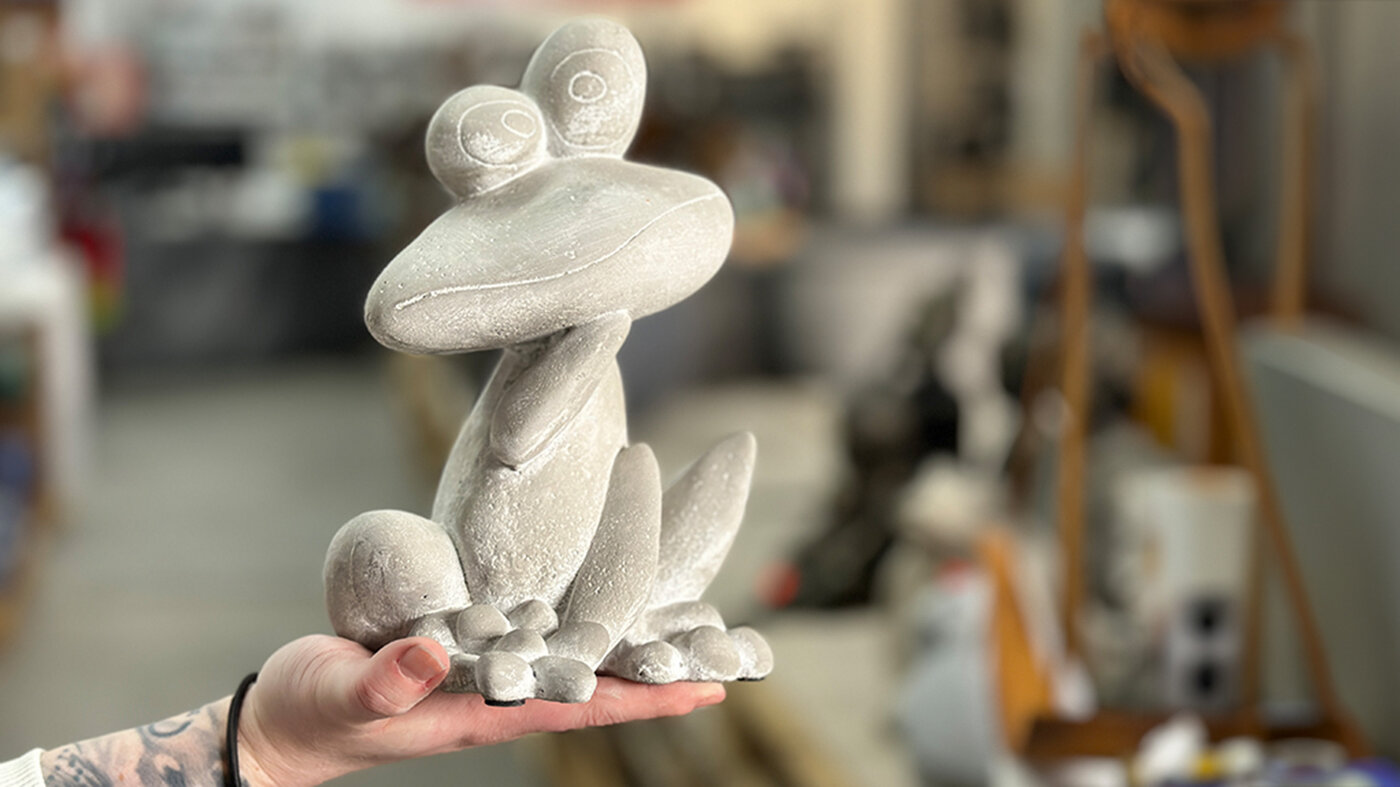 Hand hält gartec Froschfigur aus Zement als dekoratives Element für den Garten