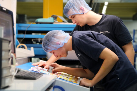 Zwei Lernende Verpackungsdrucker prüfen mit einem Fadenzähler ein Druckergebnis