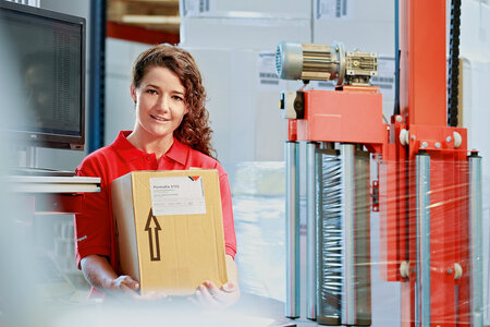 Frau trägt Karton mit Logistiketikette.