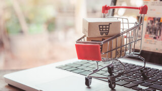 Miniatur Einkaufswagen gefüllt mit zwei Paketen auf Laptoptastatur